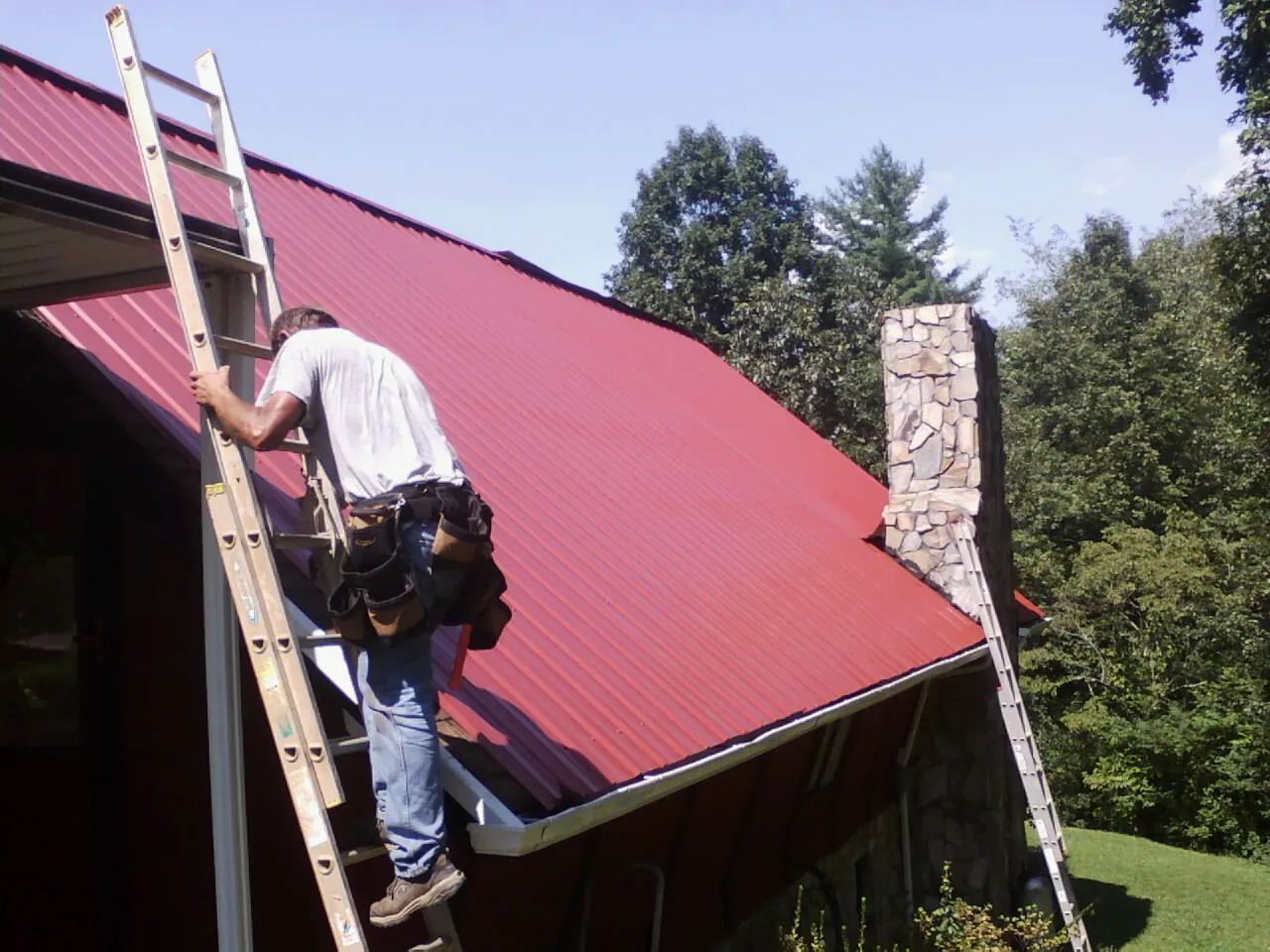 Roofer on a ladder beside a red metal roof and stone chimney in Sheffield
